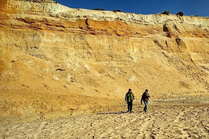Zwei Personen gehen auf Sand in der Nähe hoher, geschichteter Sandsteinfelsen