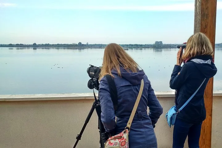 Two people birdwatching with equipment by a calm lake