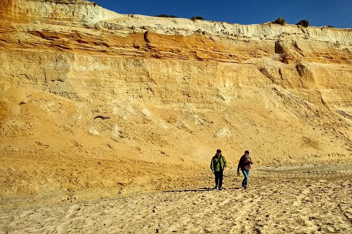 Hikers walking on a sandy area below high sandstone cliffs